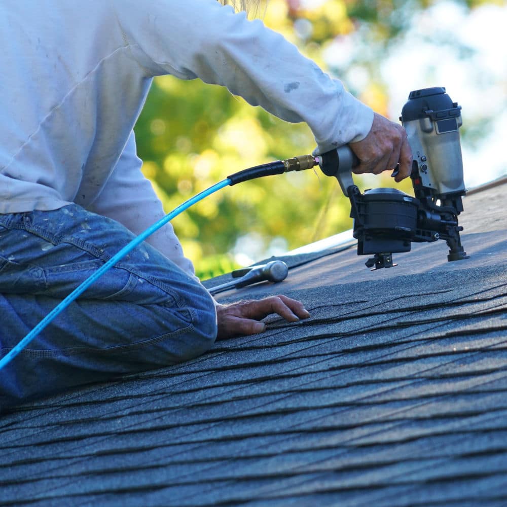 handyman using nail gun to install shingle to repair roof